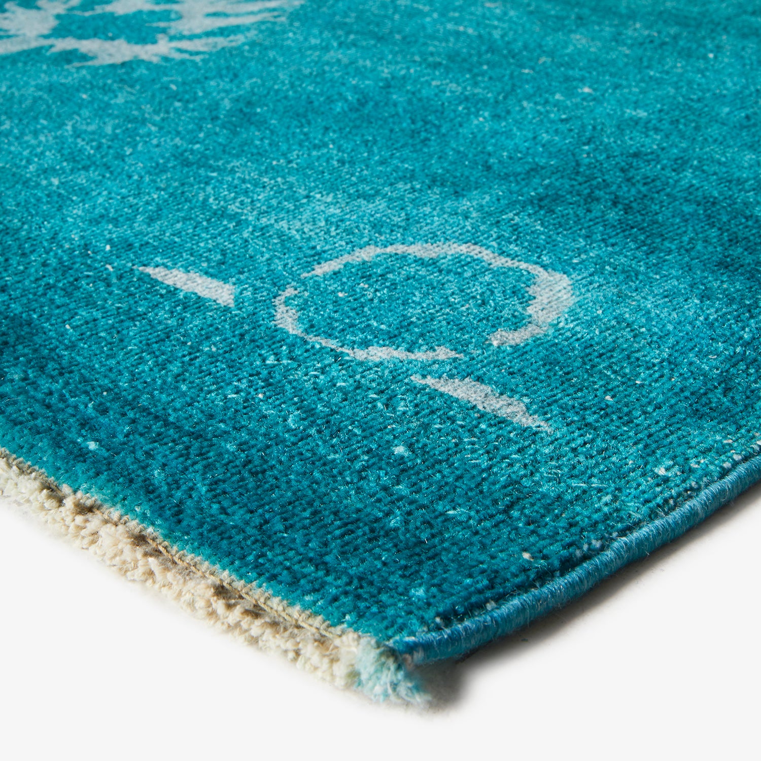 Close-up of plush turquoise bath mat with white abstract design.