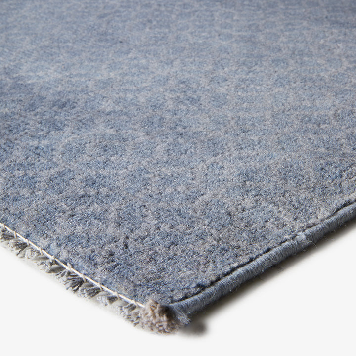 Soft blue flat weave carpet with white backing, intricate details.