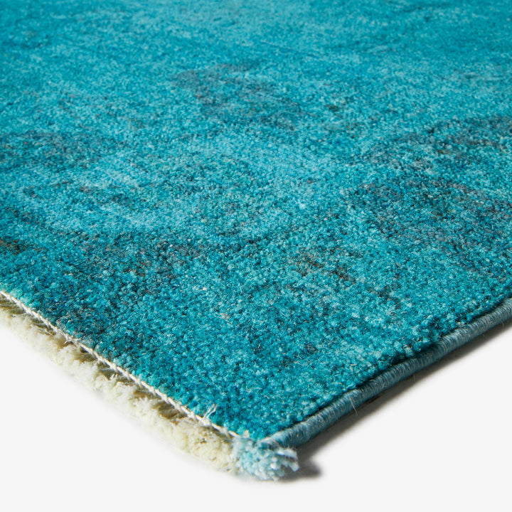 Close-up of dense teal carpet with frayed edge and texture.
