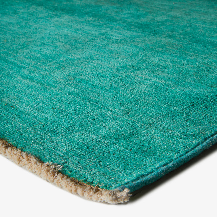 Close-up of turquoise looped carpet with beige border. Durable construction.