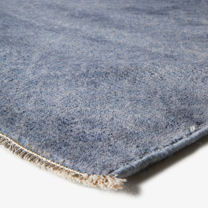 Close-up of blue plush rug with natural binding, visible crease.