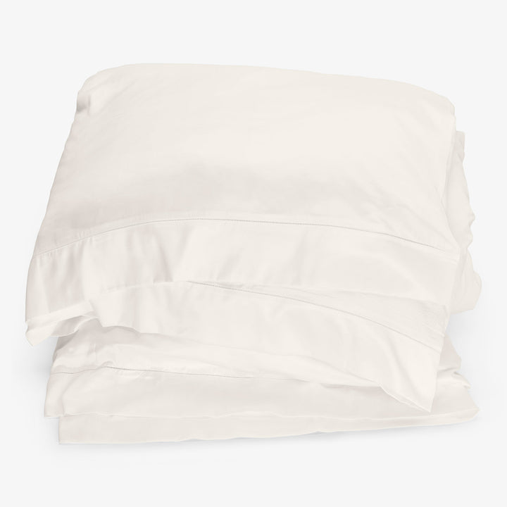 Crisp white bed linens neatly folded against white background.