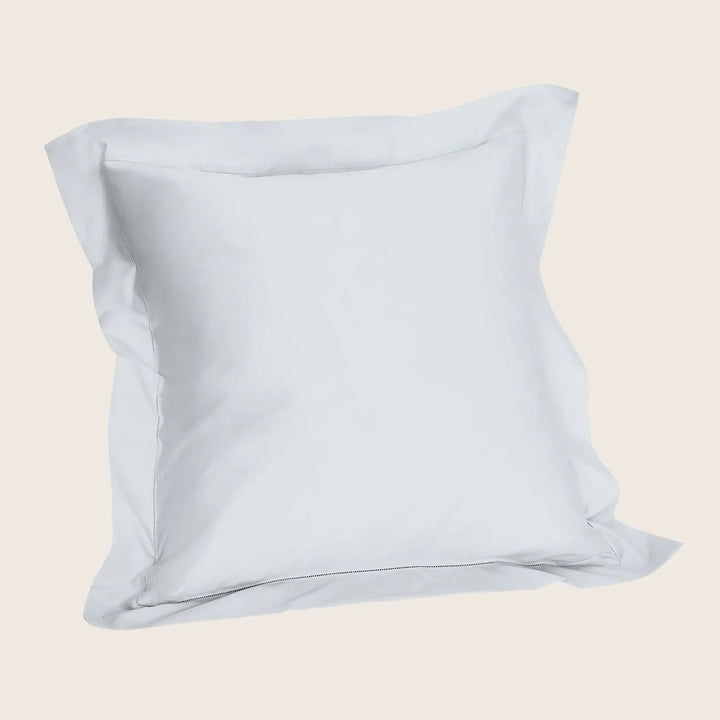 Soft white pillowcase covering square pillow on white background.