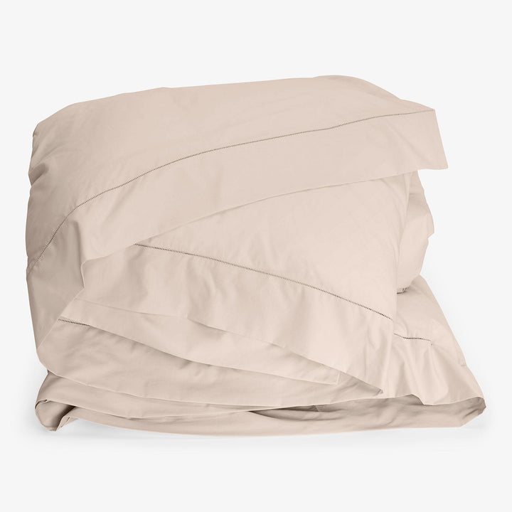 Neatly folded beige bed linens against white background in image.