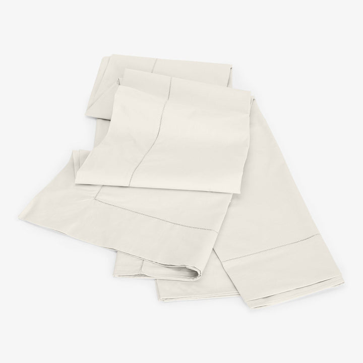 Freshly laundered cream bed linens neatly stacked on white background.