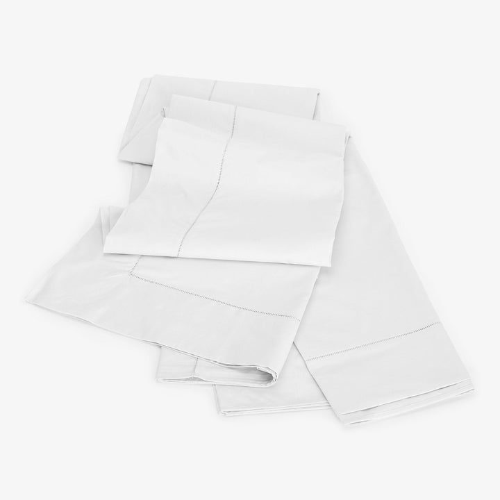 Crisply folded white bed linens on clean white background.