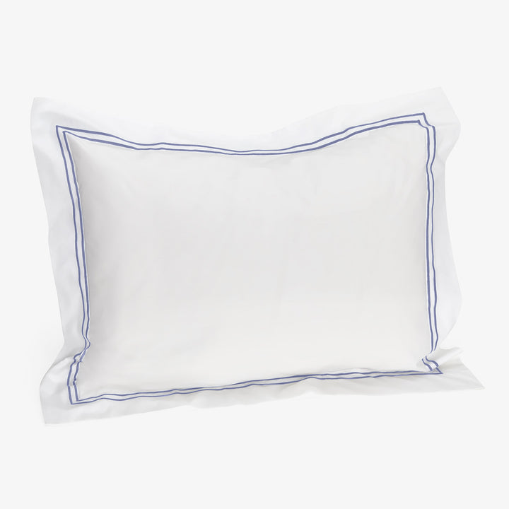 Elegant white pillow with blue border against plain background.