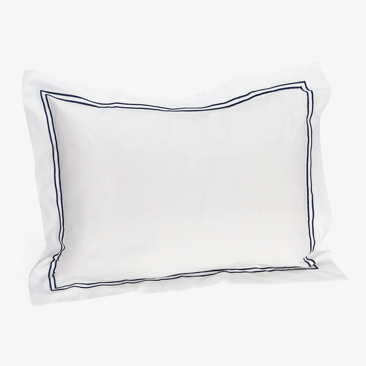 Elegant white pillow with blue embroidered border on white backdrop.