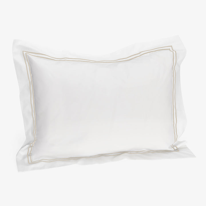 Single white pillow with beige trim, standard size for bed.