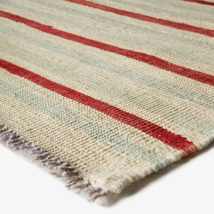 Close-up of handmade striped rug with fringe, green and red.