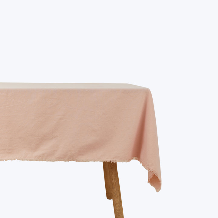 Plain wooden table with textured pink tablecloth, frayed edge visible.