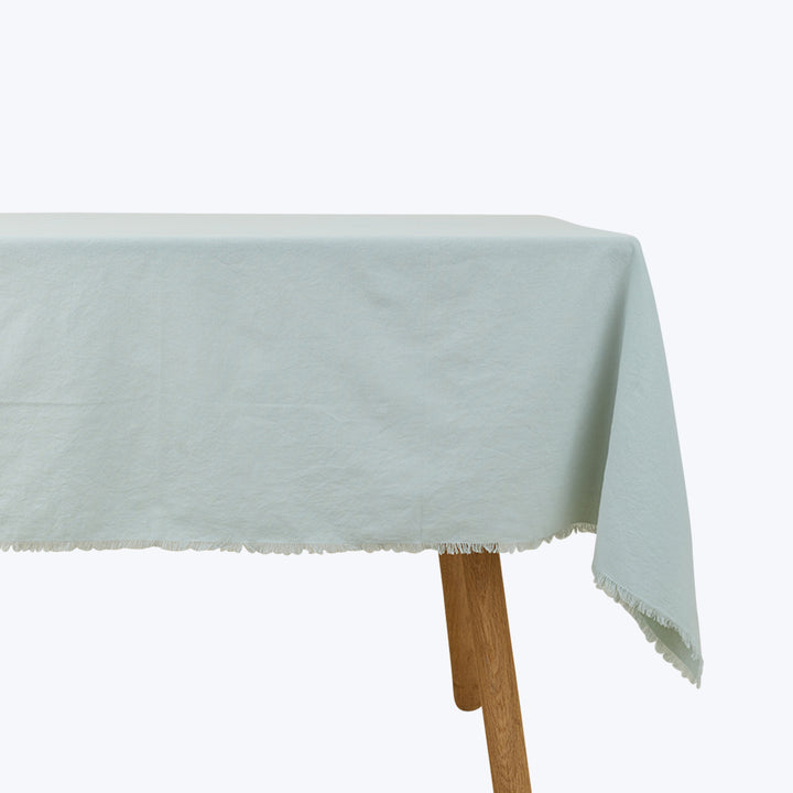 Minimalist wooden table with light tablecloth and fringed border.
