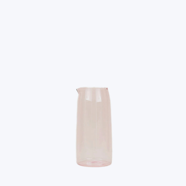 Transparent glass jug with pink hue on white background.