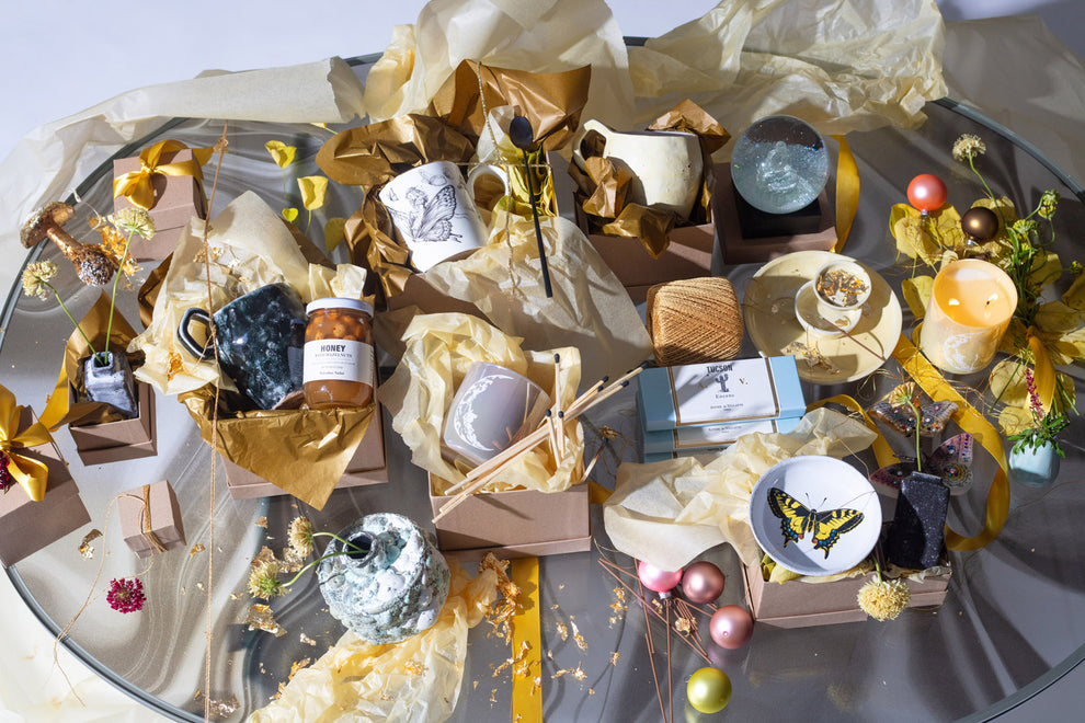 Eclectic display of artisanal gifts on reflective glass table surface.