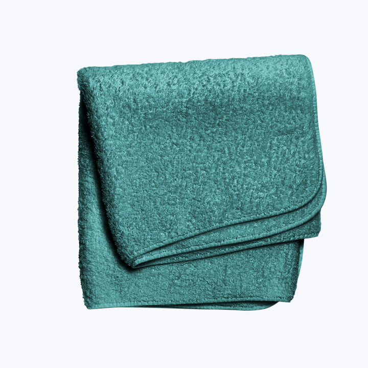 Soft teal bath towel folded neatly on white background.