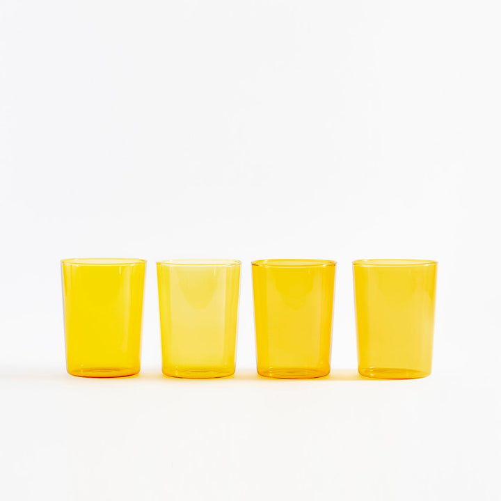 Four identical yellow glasses in straight row on white background.