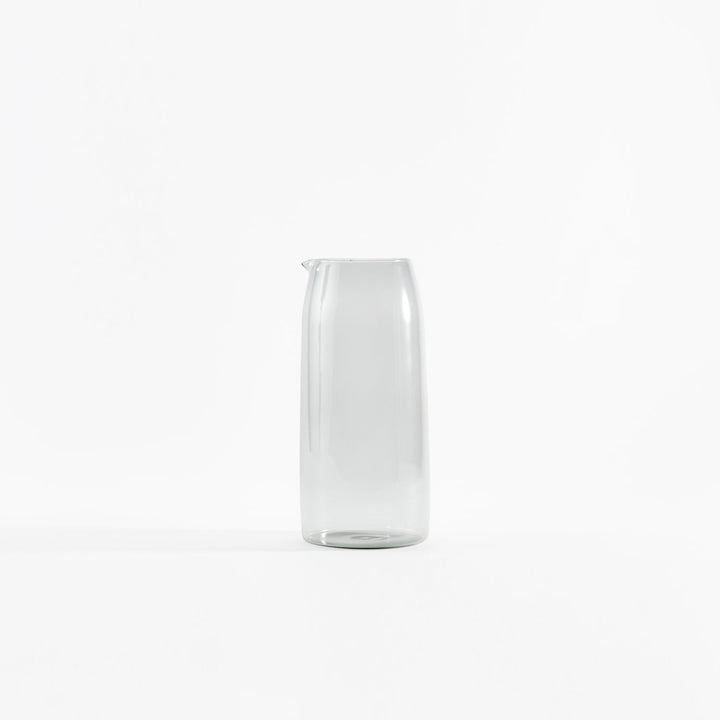 Minimalist clear glass jug against white background, empty and upright.
