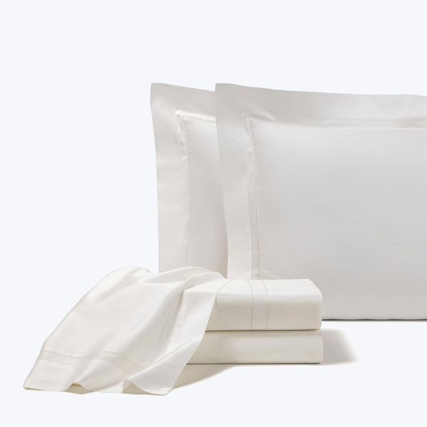 Crisp white bed linens with decorative stitching folded neatly.