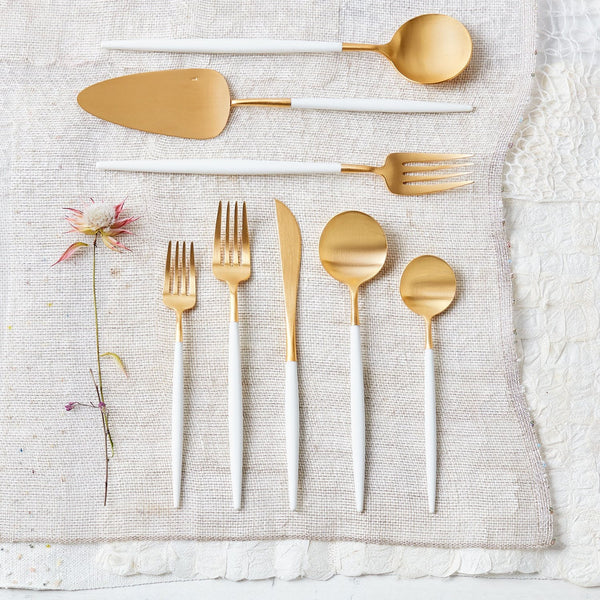 Modern gold and white cutlery set on textured fabric surface