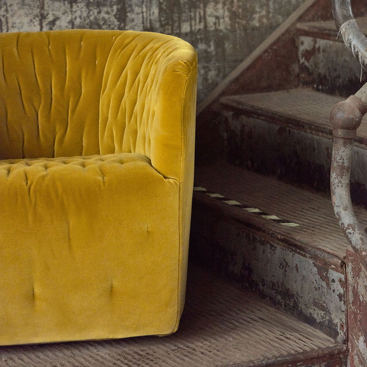 Vintage mustard yellow velvet armchair next to distressed staircase, contrasting