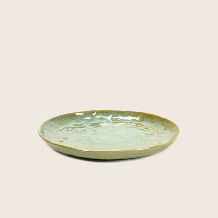 Artisanal ceramic plate with greenish-blue glaze on textured surface.