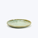 Artisanal ceramic plate with greenish-blue glaze on textured surface.