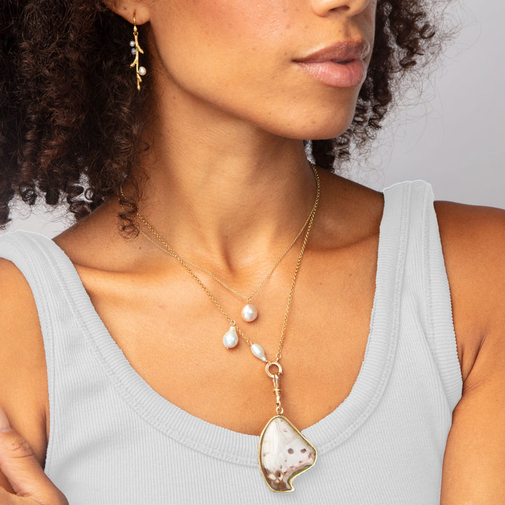 Woman in gray top wearing layered gold necklaces with pendants.
