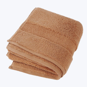 Fluffy tan towel with decorative bands stacked neatly on white background. - hover