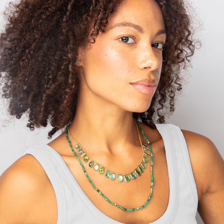 Elegant woman showcases luxurious green gemstone necklace with confident gaze.