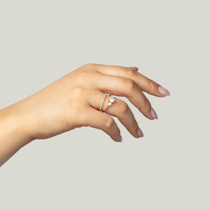 Delicate diamond ring on elegant hand against plain background.