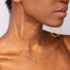 Person wearing gold hoop earrings and layered gemstone necklaces.