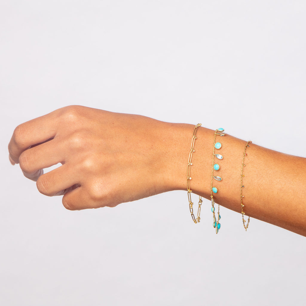 Elegant wrist adorned with three delicate gold and stone bracelets.