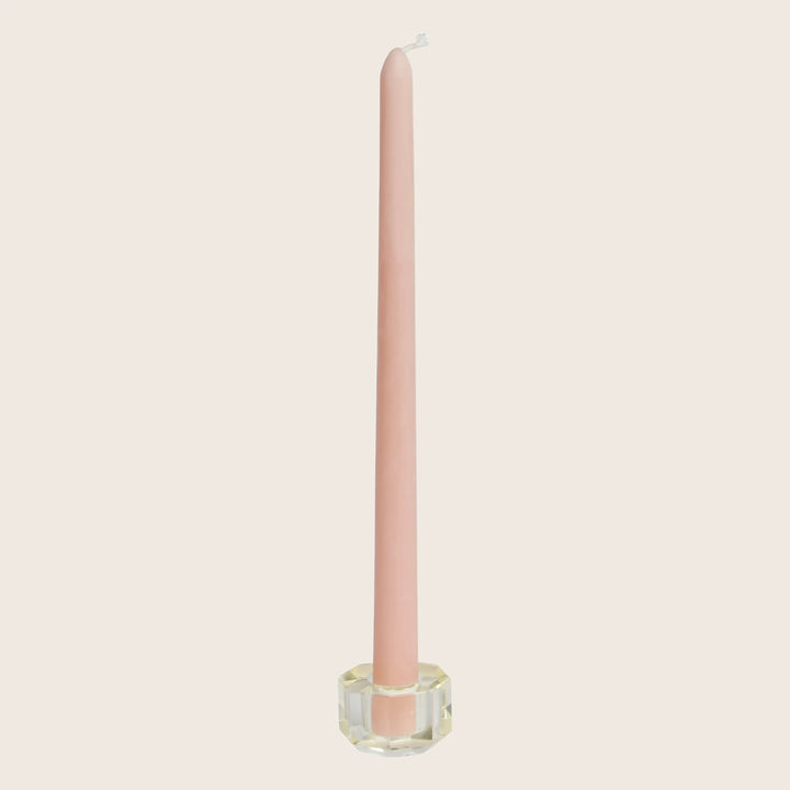 Unused tall pink candle in geometric glass holder on white background.