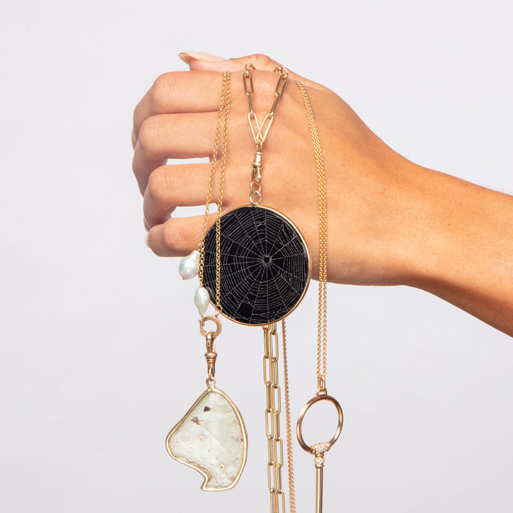 Hand holding gold necklaces with unique pendants on display.