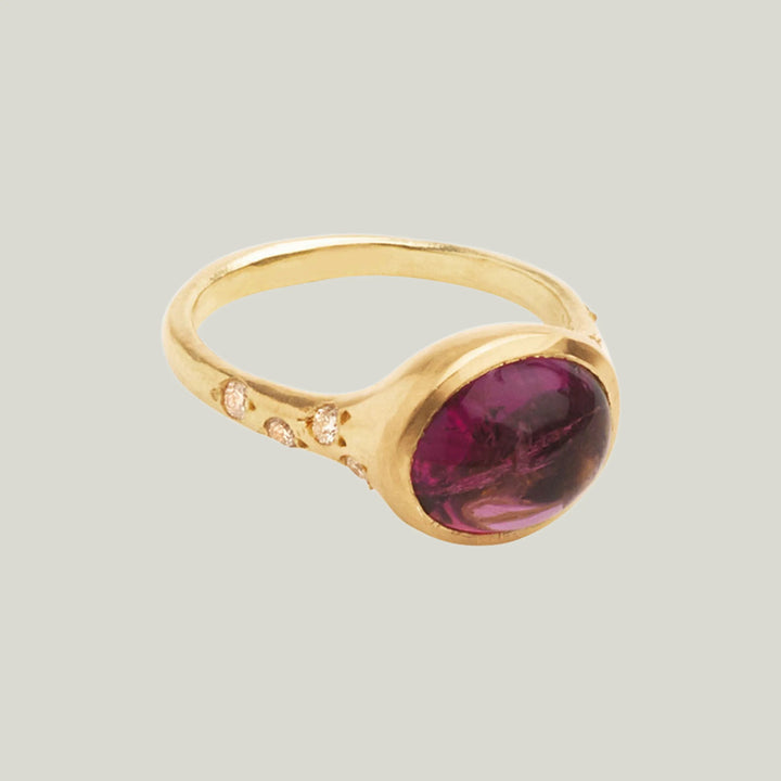 Elegant gold ring with oval red gemstone and diamond accents.