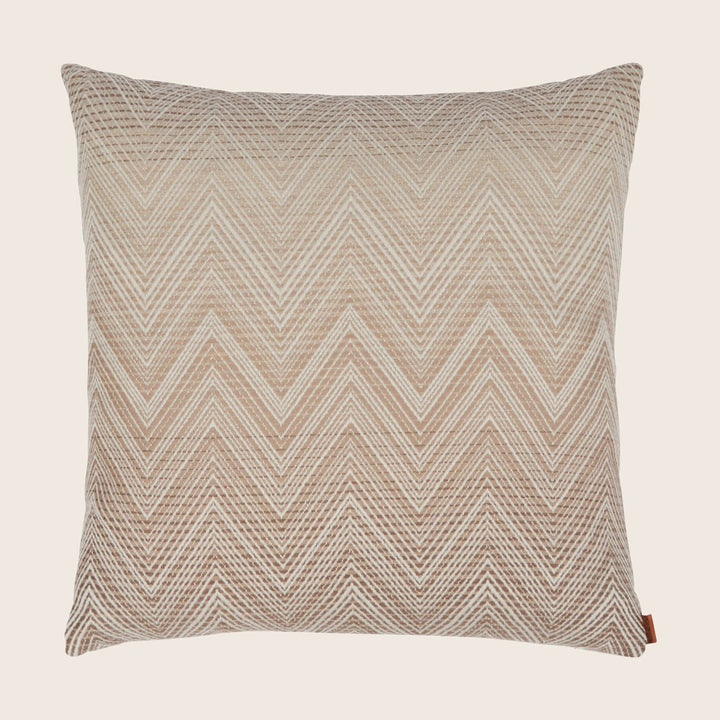 Neutral chevron patterned pillow with tag on white background.