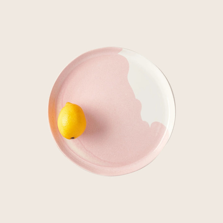 Single lemon on pink plate against white background, minimalist composition.