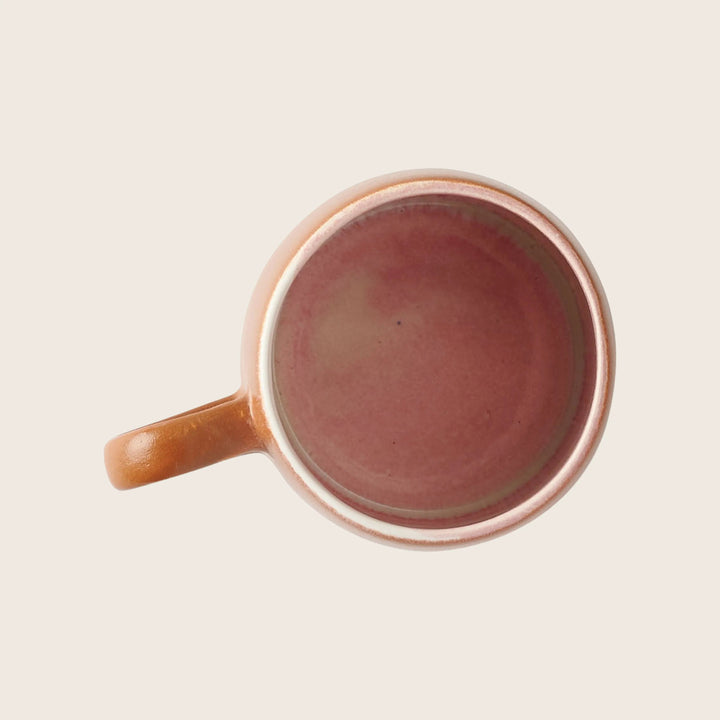 Earthy-toned ceramic mug with pink interior and orange-brown exterior.