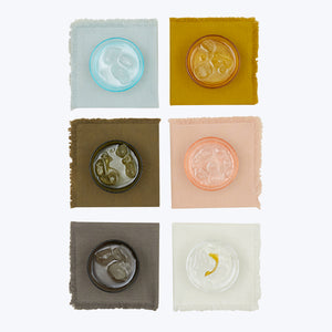 Four off-white squares, one with embossed seal, arranged symmetrically. - hover