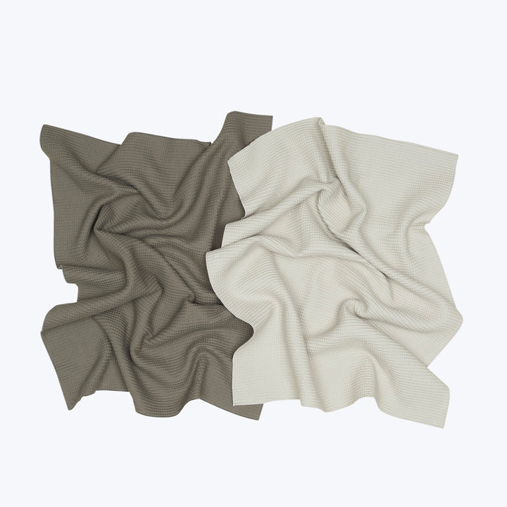 Two waffle-knit blankets in contrasting colors overlap on neutral background.