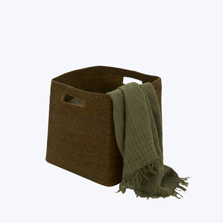 Cozy brown woven storage basket with green textured throw blanket.