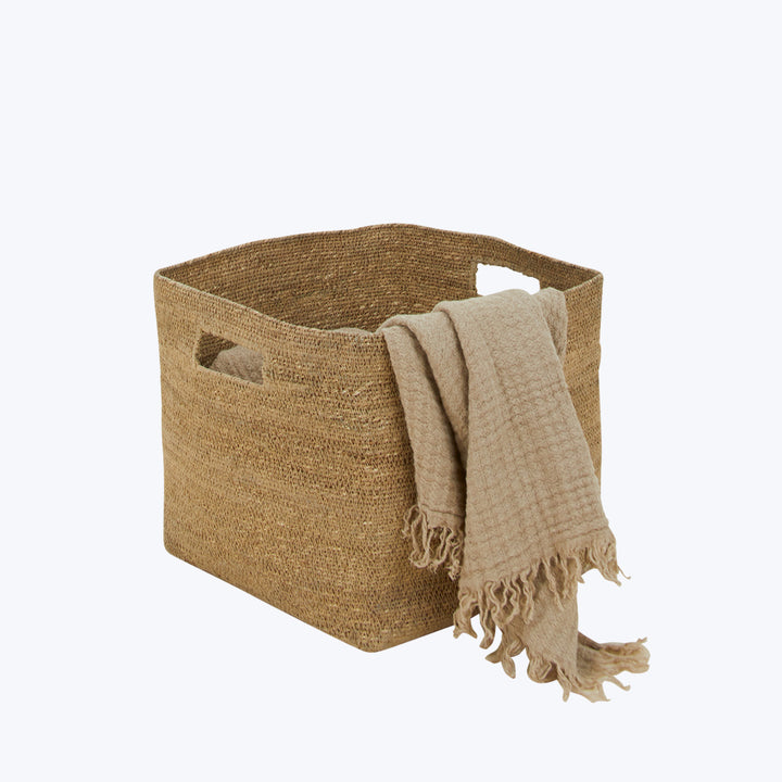 Neutral woven basket with handles, draped with fringed blanket. Minimalist decor.