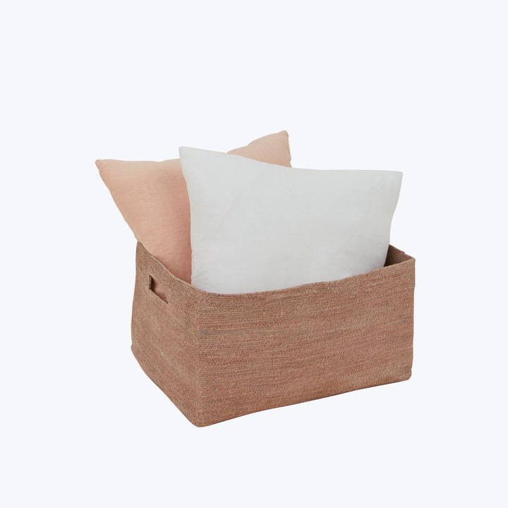 Rectangular basket with cushions in natural tones against white background.