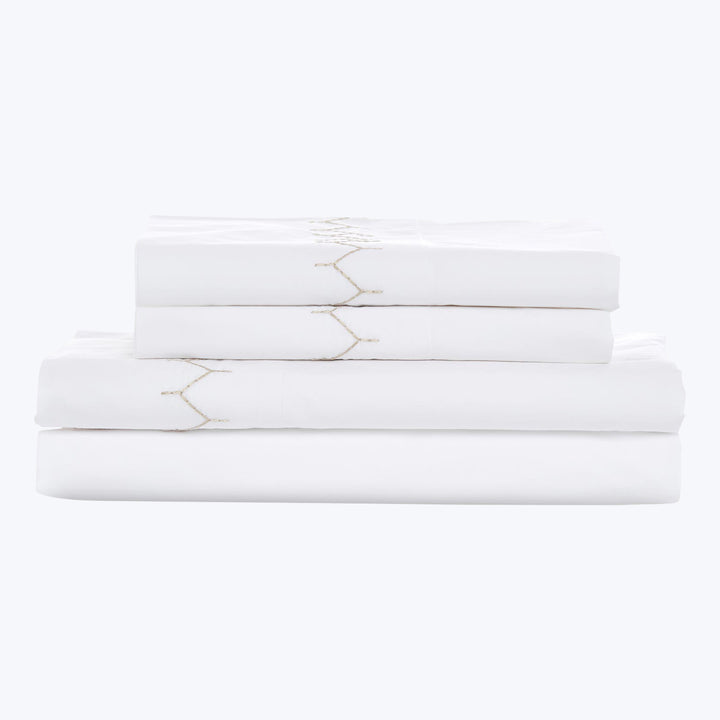 Luxury white bed sheets with gold embroidery detail stacked neatly.