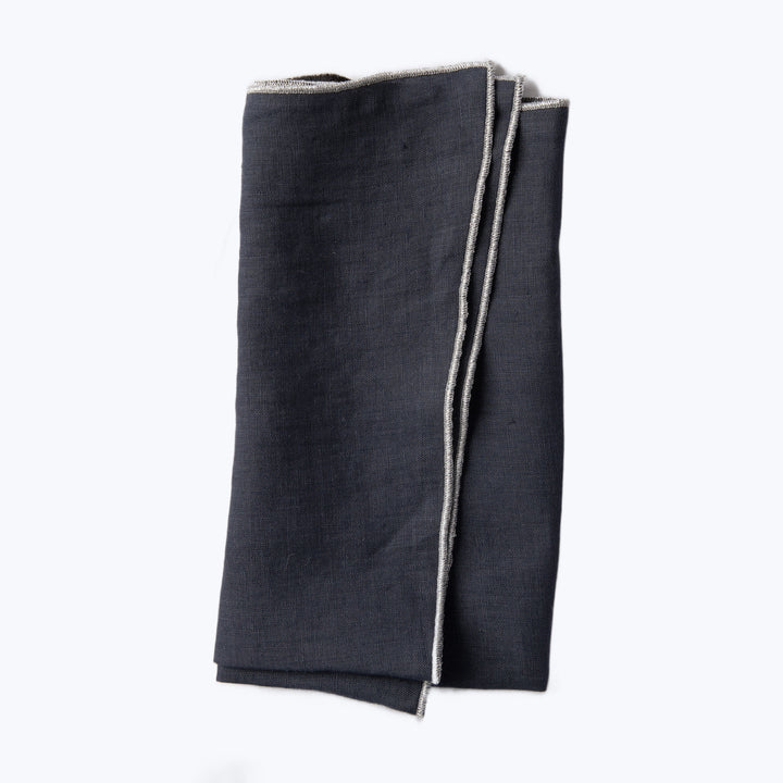 Neatly folded dark denim fabric with selvage edge on white background.