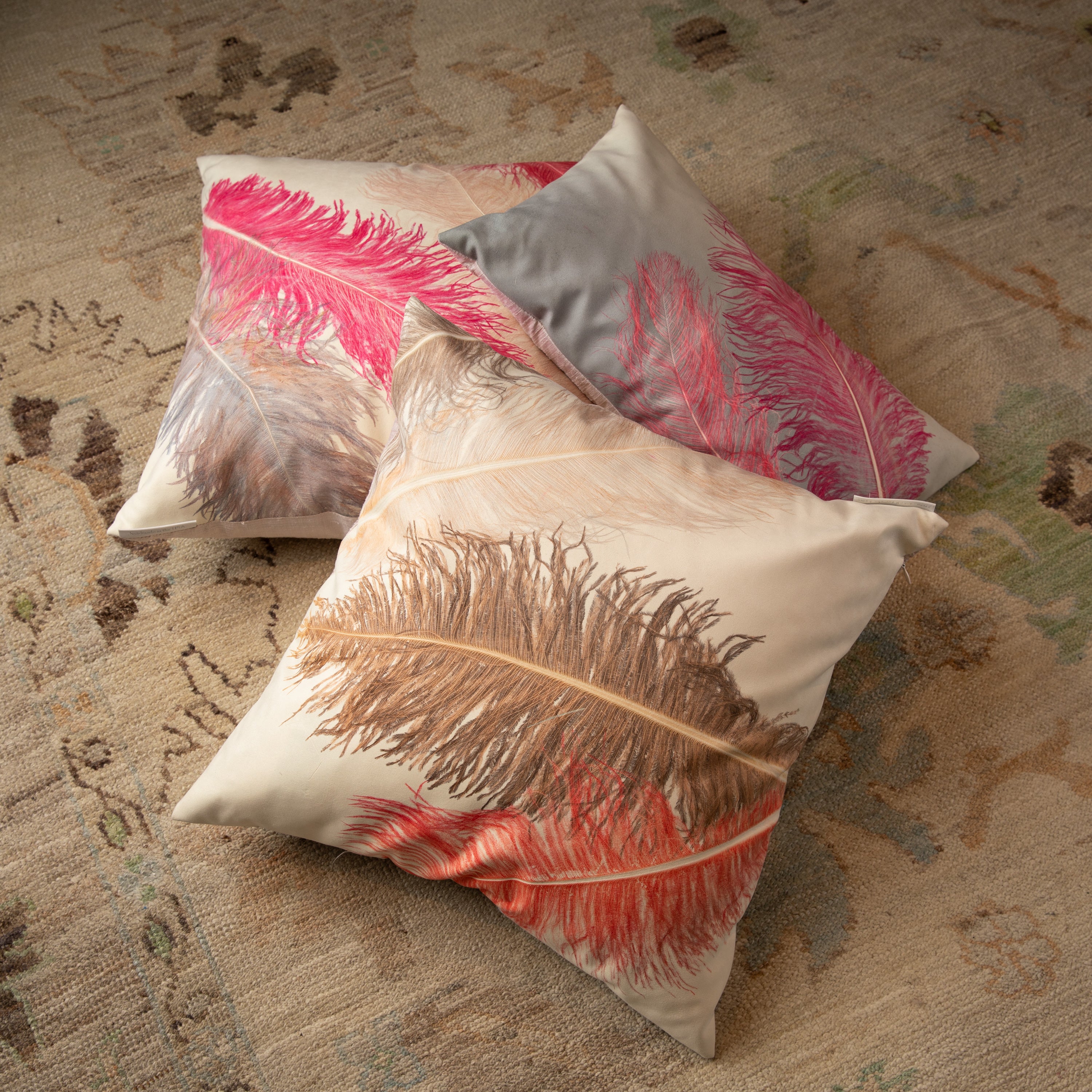 Three square decorative pillows with feather designs on carpeted floor