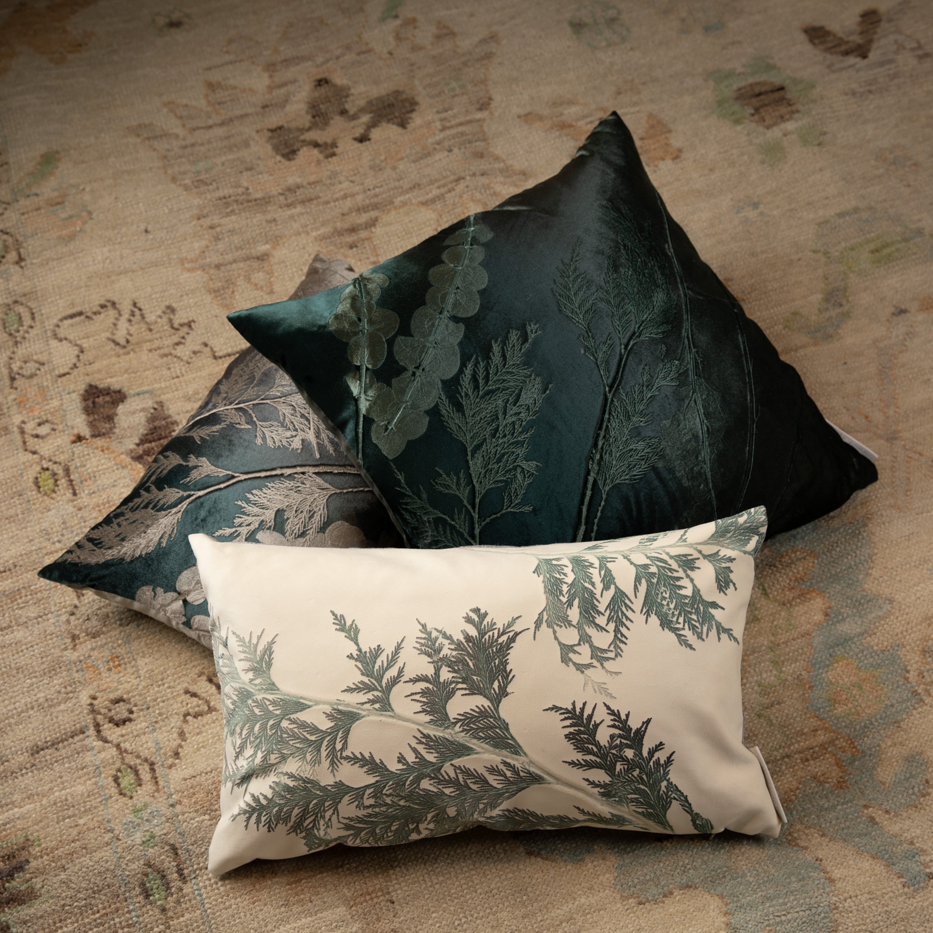 Three botanical throw pillows arranged on floral carpet for decor.