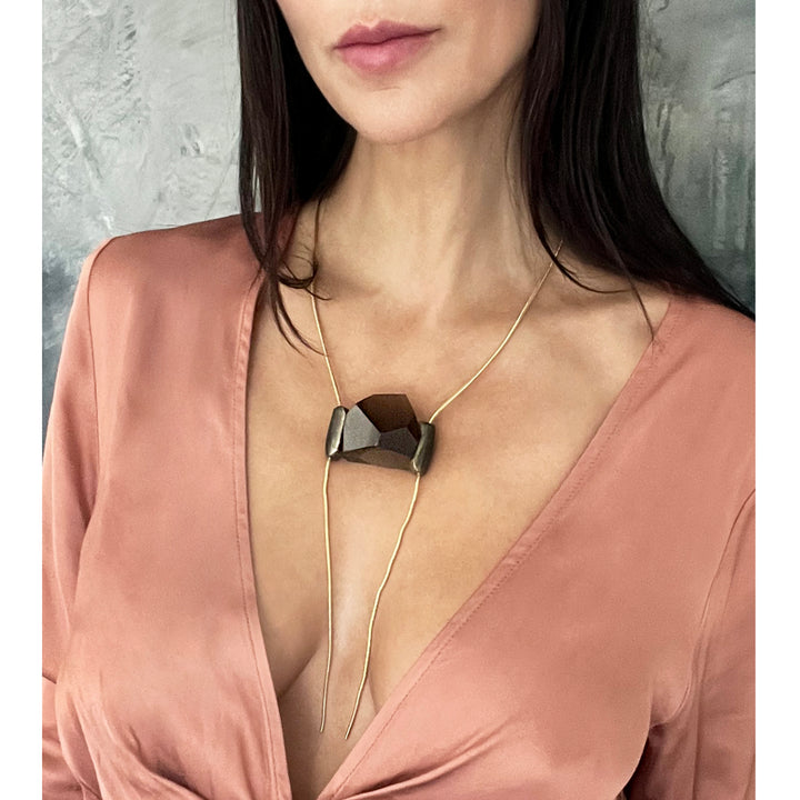 Person in peach blouse wears geometric pendant necklace, elegant fashion.