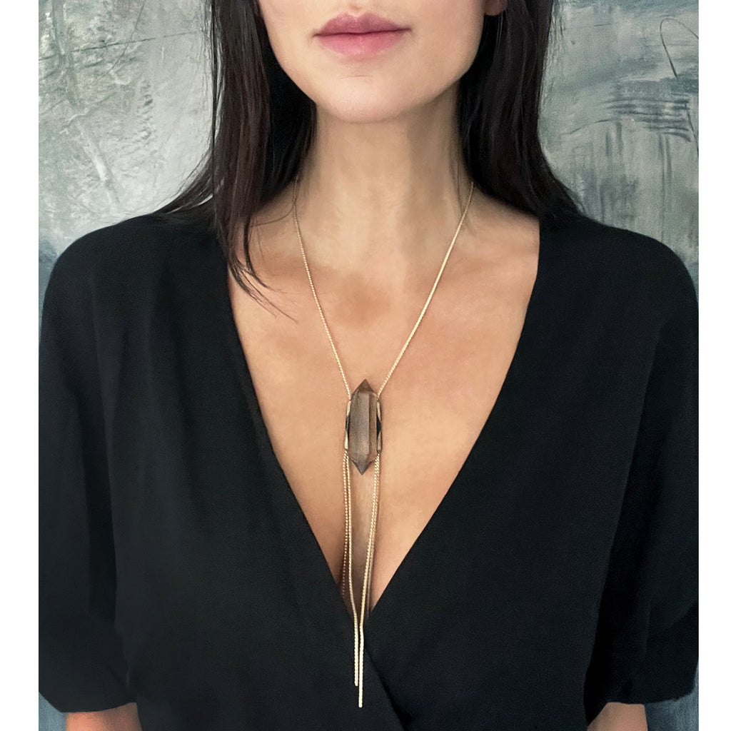 Person in black V-neck top with delicate pendant necklace.