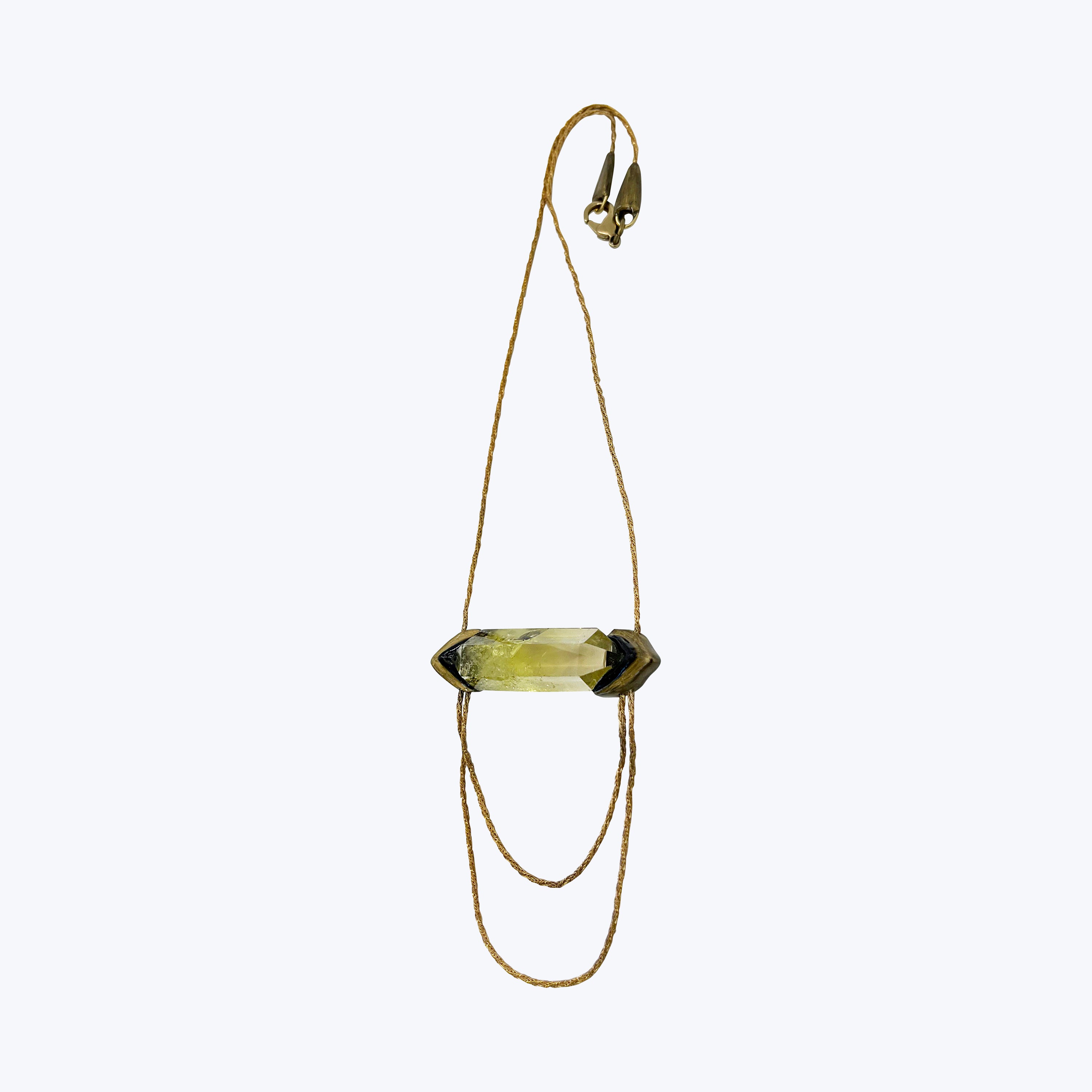 Horizontal yellow-green crystal pendant on gold chain with dark setting.